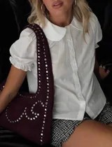 Blusa blanca de manga corta abullonada con detalle de volados, cuello bebe redondeado y cierre frontal abotonado.
