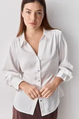 Camisa blanca de manga larga con textura suave y caída liviana, cuello camisero, puños anchos y fruncidos sutiles en los hombros.