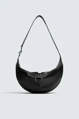 Bolso de hombro de diseño curvo en forma de media luna, confeccionado en material sintético negro. Presenta dos bolsillos frontales con cierre de cremallera y un compartimento principal con cierre. Incluye un asa de hombro integrada y detalles de costuras visibles.