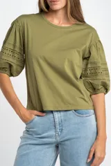 Remera negra de algodón con mangas cortas abullonadas que presentan detalles de encaje bordado y calado en los extremos.