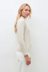 Blusa beige claro con cuello alto y mangas largas, con pequeños brillos.