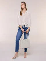 Cartera tipo tote de diseño semi-rígido y color beige, confeccionada en eco cuero. Cuenta con doble manija de hombro, base reforzada con remaches metálicos y aplique dorado con el logo de la marca en el frente.