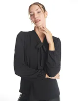 Blusa de seda fría color negro, con escote en V y lazo decorativo al cuello. Presenta mangas largas abullonadas con puños elásticos y detalles de strass aplicados en cuello, lazo y mangas.
