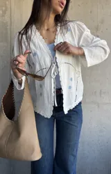 Capa blanca de manga larga con detalles bordados florales celestes y terminaciones de encaje en los bordes y la abertura frontal con tiras para atar.