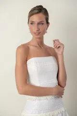 Vestido midi strapless color marfil, con diseño de paneles horizontales que combinan encaje y detalles de flecos. Presenta una falda con vuelo y movimiento.
