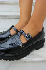 Zapato tipo guillermina en cuero charol color bordó, con suela track negra de goma, cierre con hebilla ajustable y detalle de herrajes metálicos dorados.