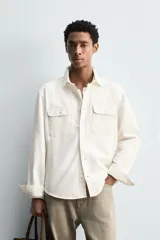 Sobrecamisa de corte regular confeccionada en denim de algodón, con cuello solapa, manga larga con puños abotonados y cierre frontal de botones. Presenta dos bolsillos frontales de plastrón con solapa y bajo con aberturas laterales.