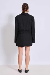 Blazer negro con solapas de muesca, corte holgado, cierre frontal con lazo y detalle de volados en los bolsillos.