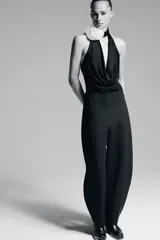 Body negro de cuello halter con escote drapeado pronunciado, detalle de flor blanca en relieve y espalda descubierta.