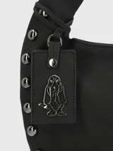 Cartera tipo hobo de la marca Hush Puppies, color negro, con diseño de asa única integrada y detalle de tachas metálicas plateadas en los laterales y la base. Incluye un tag colgante con el logo de la marca.