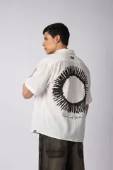 Camisa de manga corta confeccionada en una mezcla liviana de rayón y lino color blanco. Presenta un diseño de calce regular con cuello plano, botones frontales y un estampado artístico en la espalda inspirado en el sol.