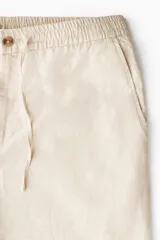 Pantalón de corte regular fit confeccionado en mezcla de lino y algodón, color beige. Presenta cintura elástica con cordón ajustable, cierre de botón y bolsillos laterales.