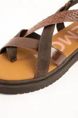 Sandalias de cuero color marrón con suela track, tiras cruzadas en el empeine con diferentes texturas y acabados, y tira ajustable al tobillo con hebilla metálica.