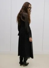 Vestido midi de gasa negro con estampado de lunares blancos, cuello alto, manga larga con volados en los puños y falda con vuelo.