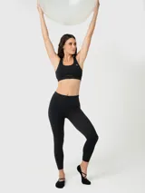 Top deportivo negro con escote redondo, tirantes anchos y un corte debajo del busto que crea una abertura. Incluye logo blanco en el pecho.