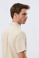 Camisa de manga corta confeccionada en mezcla de lino y algodón, color beige, con cuello camisero abotonado, bolsillo frontal en el pecho y cierre de botones.