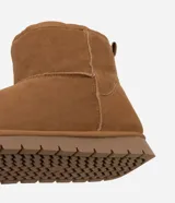 Bota de caña media color marrón, confeccionada en poliéster con acabado suave. Cuenta con interior forrado en piel sintética para mayor abrigo, tirador trasero y suela plana de goma con diseño dentado.