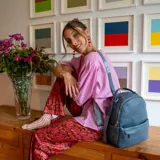 Mochila de tamaño mediano en color amarillo, confeccionada en símil cuero. Presenta un compartimento principal con cierre metálico, un bolsillo frontal con cierre y broche, y bolsillos laterales. Incluye correas regulables para la espalda, asa de mano y una correa adicional para llevar al hombro.