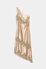 Vestido midi de satén en color beige con escote asimétrico de un solo hombro. Presenta aplicaciones de encaje a tono en el cuerpo y en el bajo, con un diseño de corte asimétrico.