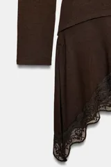 Camiseta de manga larga confeccionada en viscosa, con cuello barco y ajuste slim fit. Presenta un diseño con drapeado lateral y un bajo asimétrico decorado con una aplicación de encaje.
