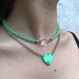 Set de dos collares: uno corto de cuentas verdes con dije de cristal facetado y otro más largo de cadena plateada con dije de corazón verde holográfico.