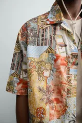 Camisa de corte relajado confeccionada en tejido ligero de algodón, con cuello bowling y manga corta. Presenta un estampado integral con motivos urbanos y tropicales en tonos cálidos.