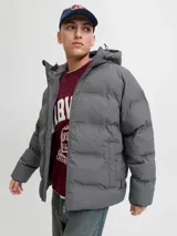 Campera puffer de color gris oscuro, con capucha integrada, cierre frontal completo y diseño acolchado horizontal. Cuenta con bolsillos laterales y acabado resistente al agua.