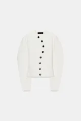 Chaqueta de punto blanco marfil, con cuello redondo, manga larga y cierre frontal asimétrico con botones negros.