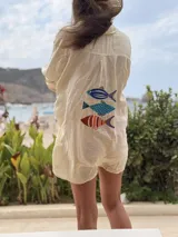 Camisa oversize de lino a rayas blancas y rosadas, con mangas largas y diseño bordado de peces en la espalda.