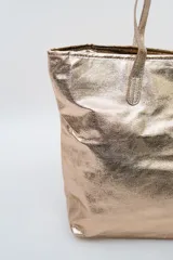 Bolso tipo tote color dorado metalizado, con doble asa de hombro y diseño amplio.