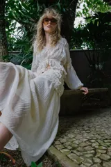 Falda midi de color crudo, con diseño combinado que presenta una parte superior de crochet con motivos florales y una parte inferior de tela fluida con textura arrugada. Incluye forro interior y cierre lateral con cremallera oculta.