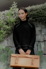 Buzo de punto color blanco con cuello alto y detalles de pespuntes decorativos en color negro en las costuras de los hombros, puños y ruedo.