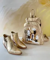 Mochila de cuero de Carolina De Cunto, modelo Lucy Natu Gold Arte. Presenta combinación de tonos naturales y dorados con textura efecto cocodrilo, diseño frontal intervenido con arte pintado a mano y bolsillo vertical con cierre.
