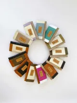 Billetera de cuero con diseño tricolor en tonos turquesa, blanco y beige, con textura tipo reptil. Cuenta con una solapa frontal con cierre de broche y una etiqueta de cuero con el logo grabado.