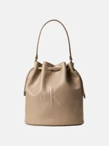 Cartera tipo bucket de Calvin Klein en color beige, confeccionada en poliuretano con asa superior, cierre con cordón ajustable y monograma de la marca grabado en el frente.