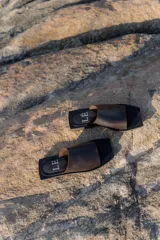 Sandalias planas con punta cuadrada, base negra y capellada de cuero marrón con textura trenzada.