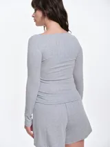 Remera de manga larga entallada en tejido pointelle, con escote bote y detalle de pequeño lazo central. Presenta un acabado con borde picot en el escote.