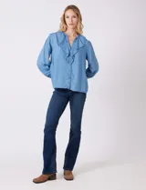 Blusa de lyocell color azul claro, con escote en V y volados en el cuello y la parte frontal. Tiene mangas largas con puños elásticos y cierre de botones en la parte delantera.