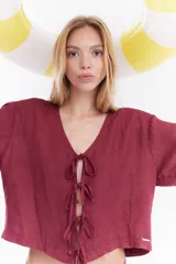 Blusa de lino color bordó, de manga corta, con escote en V y cierre frontal mediante lazos para atar.