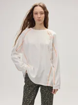 Remera manga larga de algodón color crudo, con cuello redondo y calce holgado. Posee costuras a la vista en color naranja y un delicado bordado con la frase "the flower edit" sobre el hombro izquierdo.