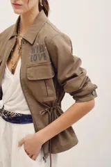Campera estilo militar color verde militar, con cierre frontal, bolsillos con solapa en el pecho y cordón ajustable en la cintura. Presenta el texto "WILD LOVE" estampado en el pecho.
