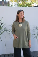 Sweater de punto color verde oliva, con cuello redondo, mangas largas y bolsillos frontales tipo parche. Presenta un corte holgado y largo, con terminaciones acanaladas en el ruedo y los puños.