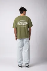 Remera de algodón con estilo deportivo, color verde oliva con efecto de lavado gastado. Presenta el número 15 estampado en blanco en el frente y detalles de costuras con vivos blancos en los hombros. Posee cuello redondo y corte holgado.