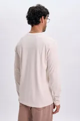 Remera manga larga de color beige, con cuello redondo y pequeña estampa de texto en el pecho.