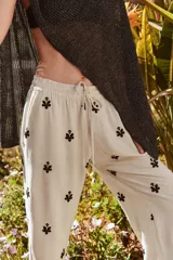 Pantalón color crema de tiro medio con cintura elástica ajustable y bolsillos delanteros. Presenta bordados florales en negro y corte ancho.