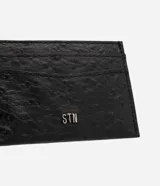 Tarjetero de poliuretano color negro con textura símil cuero de avestruz, múltiples compartimentos para tarjetas y aplique metálico con el logo de la marca en el frente.