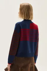 Polera de tejido de punto con diseño multicolor que combina rayas horizontales en tonos azul y bordó, flecos decorativos en el frente y un bordado central en forma de trenza. Presenta cuello semi polera, mangas largas y puños acanalados.