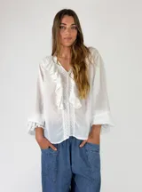 Blusa de algodón blanca con escote en V, mangas largas amplias y detalles de volados con encaje bordado en el frente.