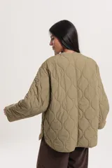 Campera capitoneada color verde oliva, con cuello redondo, cierre frontal con botones a presión, bolsillos laterales y aberturas laterales con botones.