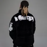 Campera de textura afelpada en color negro, con cuello alto y cierre frontal. Presenta letras bordadas en color blanco en la espalda y en las mangas. Cuenta con ajuste en la cintura y un corte regular.